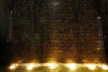 Decorative waterfall with yellow light lighting up from under the water.