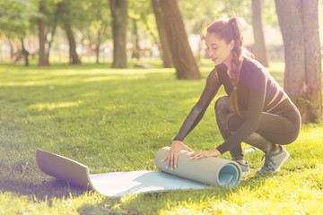 Young Caucasian woman braids a Mat for yoga in the Park at sunrise