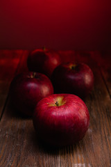 Red apples on dark wood planks and background in red light.