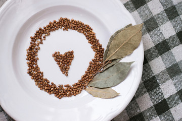 Buckwheat on a white plate with a bay leaf. View from above. Love is in every grain.