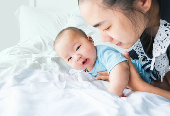 Selective focus a newborn asian cute baby boy wore blue Infant bodysuit playing with mother on the bed,Charming fat child 5 month old enjoy and happy