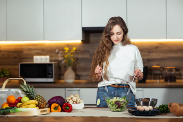 Healthy Food - Vegetable Salad. Diet. Dieting Concept. Young curly woman preparing vegetable salad in her kitchen. Healthy lifestyle concept, beautiful smiling woman mixed vegetable.
