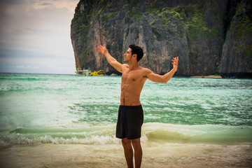 Muscular young man on the beach, with arms open enjoying the sensation of freedom in front of rising or setting sun