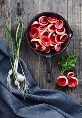 Mushrooms from the forest on a wooden background, in a frying pan. Sarcoscypha edible spring mushroom with parsley, garlic and onions. Flat lay