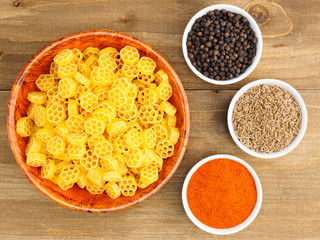 Raw pasta in a bamboo bowl and spice set: red chili pepper, black pepper, cumin. Healthy eating concept