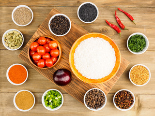 Raw white round grain rice in a bamboo bowl, tomato and spice set: red chili pepper, masala, black pepper, cumin, fenugreek, cloves, green and red onion, fennel