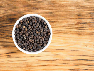 Black pepper in white bowl on brown wood background with copy space