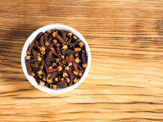 Spice cloves in white bowl on brown wood background with copy space. Healthy eating, ayurveda, naturopathy concept