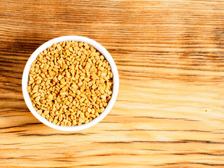 Spice fenugreek in white bowl on brown wood background with copy space