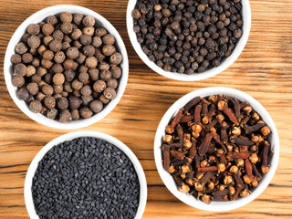 Spice black pepper, cloves, black cumin, allspice in white bowls on brown wood background. Healthy eating, ayurveda, naturopathy concept