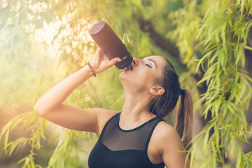 Young woman drinking water while doing sports in the Park