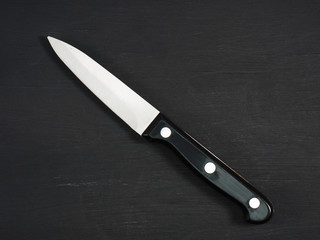 Medium sharp kitchen knife with black handle on a black wooden board