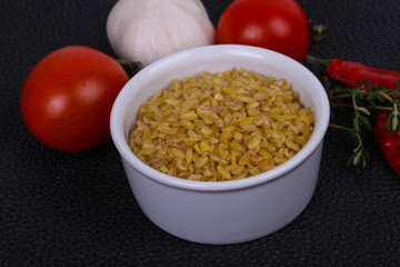 Raw bulgur in the bowl with tomatoes and garlic