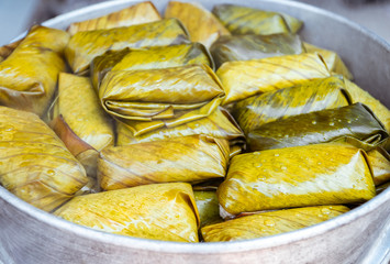 Close up view. Porridge rice wrapped in banana leaves pile in steamer with vapour smoke. Is traditional dessert found in rural areas of Thailand.