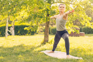 Young Caucasian woman doing yoga in the Park. He spreads his hands in different directions. Warrior pose