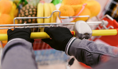 Coronavirus 2020 pandemic. Close up of man hands in medical disposable gloves with a supermarket cart. People goes to the market to buy food during quarantine. Covid 19 epidemic over the World