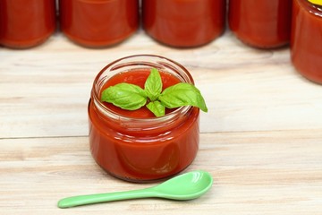 Homemade preserved  ketchup and basil leaves.  Jars of fresh ketchup at the background.