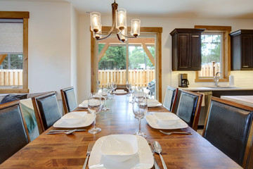 DIning room close up with white plates, glasses, wooden table and leather black modern and midcentury chairs.