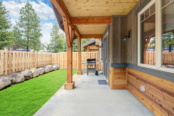 Small new back yard with wooden house and fence, fresh grass and BBQ on the concrete porch.