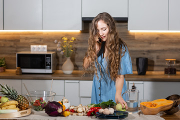 Healthy Food - Vegetable Salad. Diet. Dieting Concept. Young curly woman preparing vegetable salad in her kitchen , talking on the mobile phone and smiling while . Healthy lifestyle concept.