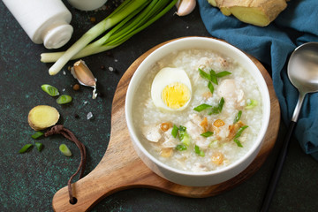Arroz Caldo Soup. Hot soup with ginger chicken rice and garlic in a bowl on a dark countertop.