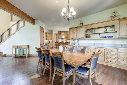 Massive dining room interior table with bright large room and stone fireplae.Dark wide hardwood floor,