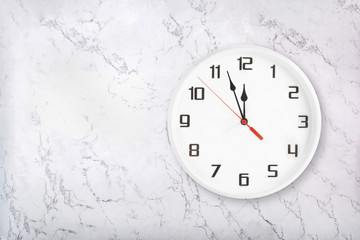 White round wall clock on white natural marble background. Almost twelve midday or midnight concept