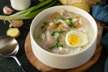 Arroz Caldo Soup close-up. Hot soup with ginger chicken rice and garlic in a bowl on a dark countertop.
