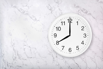 White round wall clock on white natural marble background. Eight o'clock. 8 a.m. or 8 p.m