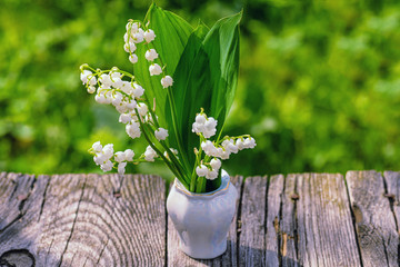 Bouquet of spring flowers standing in a vase on a wooden table with copy space.Lily of the valley. Flower Spring Sun White Green Background Horizontal. Ecological background Blooming lily.