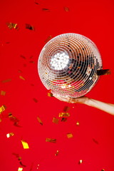 Female hand holds a disco ball on a bright red background and gold glitters fly