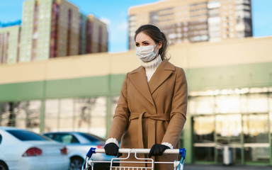 Coronavirus 2020 pandemic. Young woman in a disposable facial mask and medical gloves with a shopping cart. Girl goes to the supermarket to buy food during quarantine. Covid 19 epidemic over the World