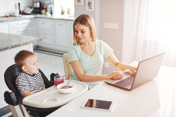 Young mother looking at computer while feeding baby