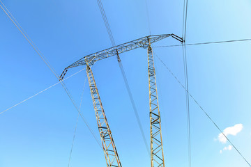 Looking up tall steel power pylons with electric cables against blue sky