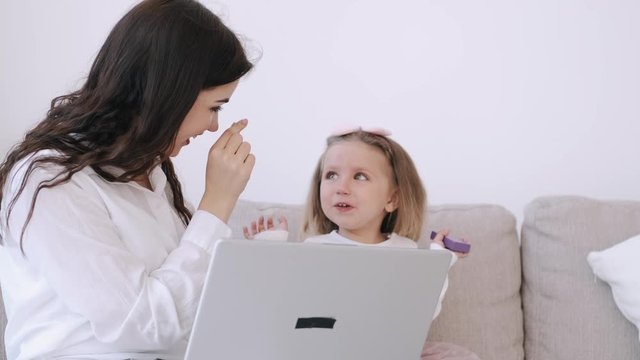 The pretty mother and her child girl are studying with a laptop. The mother is teaching heer kid. The girl is getting along with the parent typing on the keyboard and watching something on hte laptop