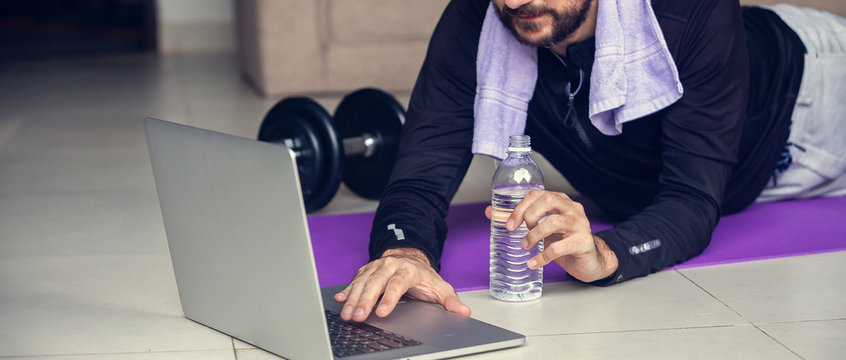 Young man exercising and working out online with laptop or phone at home during covid-19 pandemic quarantine. Sports and healthy lifestyle concept