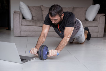 Fototapeta na wymiar Young man exercising and working out online with laptop or phone at home during covid-19 pandemic quarantine. Sports and healthy lifestyle concept