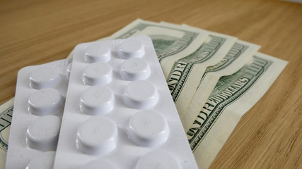 Pills on the table in white plastic and dollars on the table.