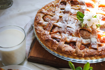 An apricot pie and a glass of milk stood on the table. Flowering branches of cherry.