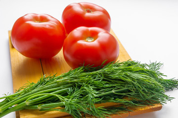 Tomatoes and dill lie on a cutting Board on a white background.