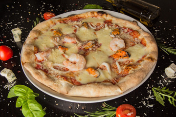 Pizza with prawns frutti di mare - on a black table, with scattered spices and ingredients. Photo for the menu.