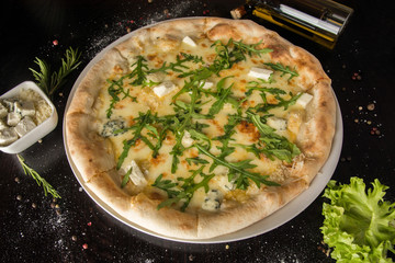 Four cheeses pizza - with arugula. On a black table with a sprinkled row of spices and ingredients. Photo for the menu.
