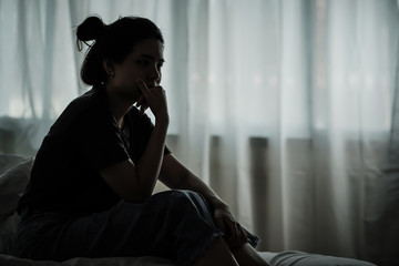 Depressed woman sitting alone on the bed feel stress sad and worried in the dark bedroom and low...