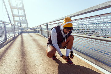 Urban sport man tying shoelaces on bridge