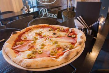 Pizza on the table - in the interior of the pizzeria, next to the menu without text