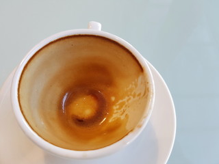 Coffee stains that remain in the cup after drink. A white coffee cup with an empty saucer on a white table Coffee is both beneficial and harmful to the body.Should drink no more than two glasses/day 
