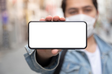 Young man stretches his smart phone to the camera while wearing a protective mask
