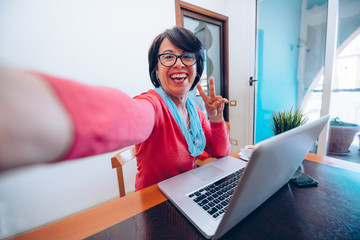Sixty year old female teacher wearing headphones taking a selfihaving online class via video chat...