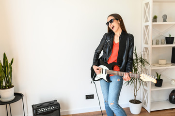 Home leisure with fun. A young beautiful woman in sunglasses and in leather jacket is playing an...