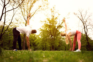 Fit young man and woman exercising in park. Smiling caucasian couple doing workouts on grass on sunny morning.